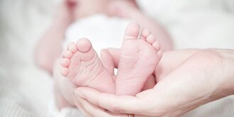 A disembodied hand holds the small feet of a young baby. 