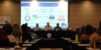A centered visual of the four panelists speaking at a table with the audiences on both sides of the aisle.