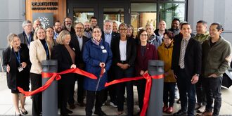Large group of people with woman in center cutting a red ribbon