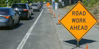 Road work zone with orange ODOT sign that reads "road work ahead". There's a line of cars stopped waiting to slowly drive through the work zone.