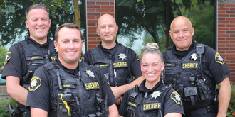 Smiling officers standing in a group in front of a brick building and landscape