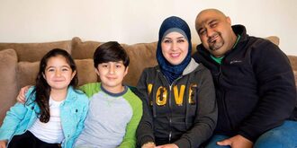 A picture of Ahmed and his wife and two children on the couch smiling for the camera.