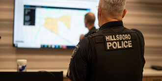 Back of a man wearing a hillsboro police uniform looking at a large screen showing a map