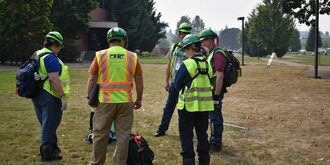 Five people in bright yellow vests and hard hats stand in a circle