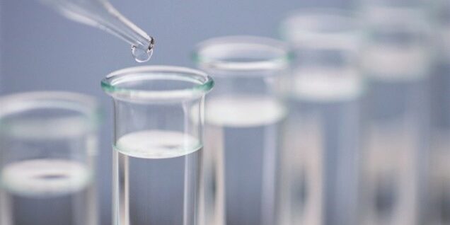 A glass pipette dispensing a drop of water into a row of test tubes