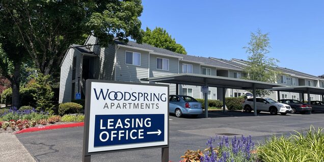 An external view of Woodspring Apartments' entrance and its leasing office sign