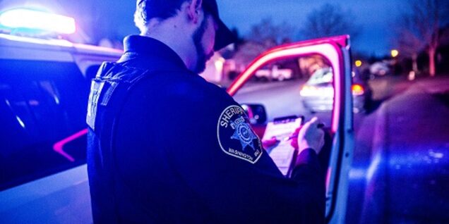 Patrol deputy standing alongside a Sheriff's Office vehicle at night while writing in a notebook.  