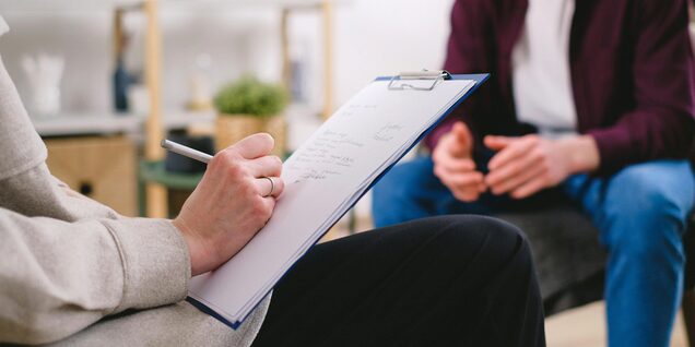 A person writes on a clipboard in an intake session with another person