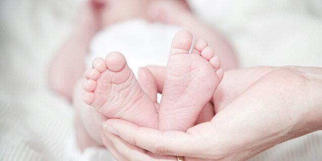 A disembodied hand holds the small feet of a young baby. 