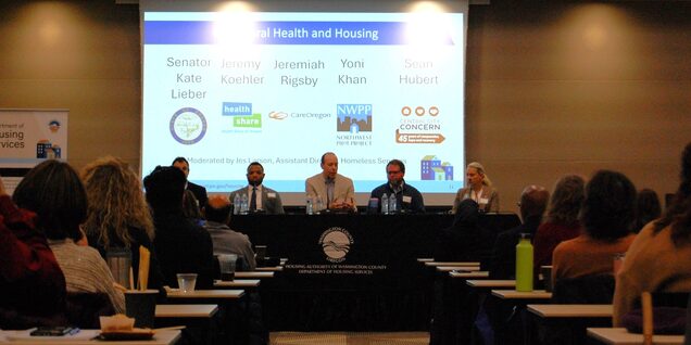 A centered visual of the four panelists speaking at a table with the audiences on both sides of the aisle.