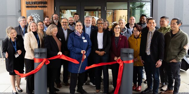 Large group of people with woman in center cutting a red ribbon