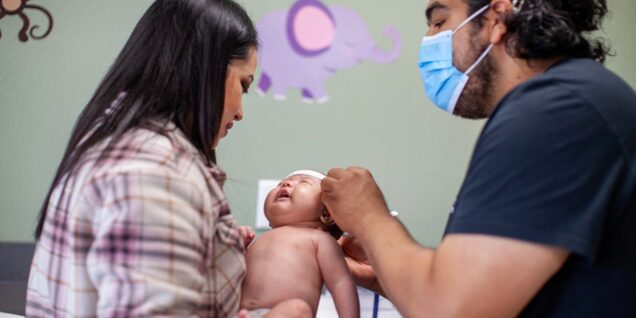 Mom holds little baby while male staff measures head