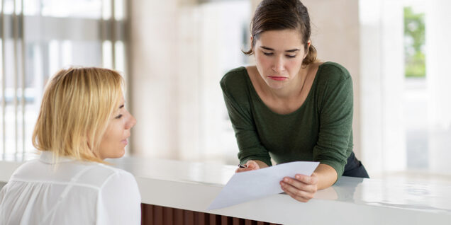 Person talking to another person while pointing to a paper document