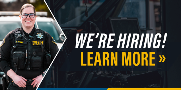 A smiling deputy standing in front of a patrol vehicle beside text that says we're hiring