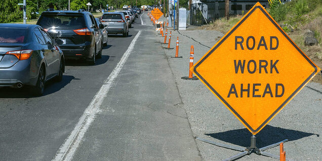 Road work zone with orange ODOT sign that reads "road work ahead". There's a line of cars stopped waiting to slowly drive through the work zone.