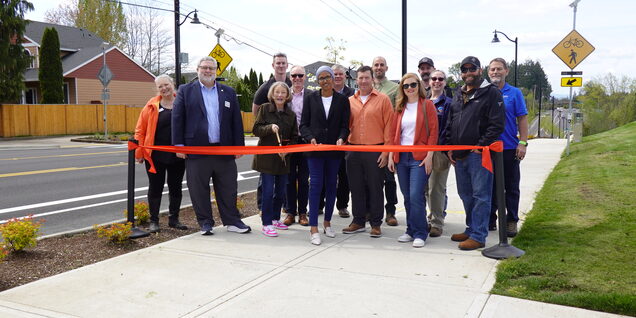 County officials and staff gather to cut a red ribbon stretched across the multiuse path along Springville Road