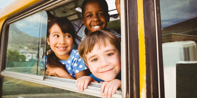 Three kids smiling out the window of a school bus