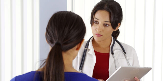 Female doctor holding a chart talks to a patient