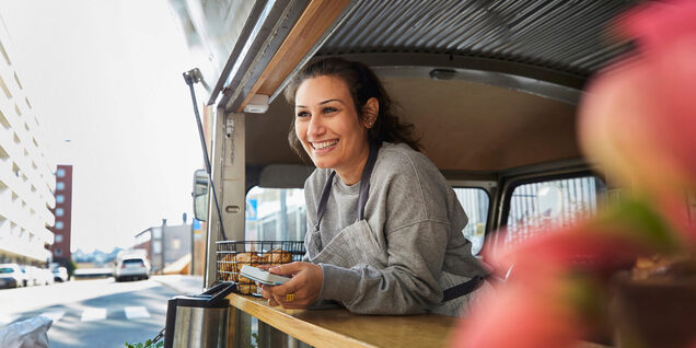 A woman smiles at a patron from the window of a food truck