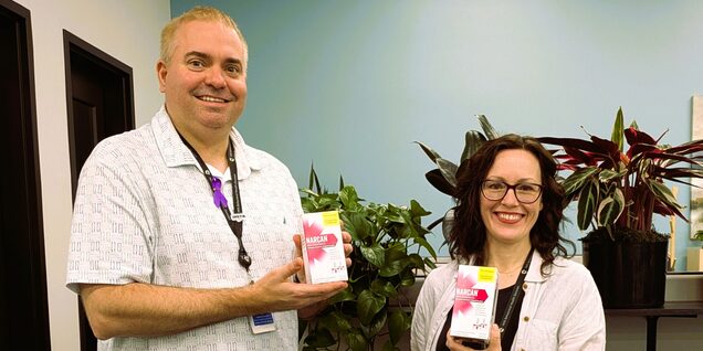 Man and woman smiling holding boxes of naloxone