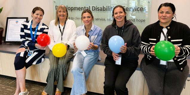 Five women each holding a different color balloon