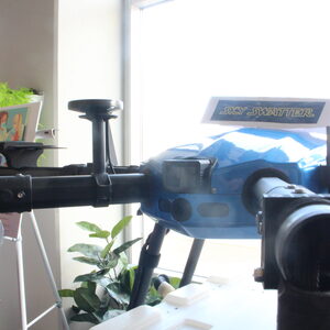 A blue drone with black rods extending out from it. A sign saying "Sky Swatter" rests right on top of it. 