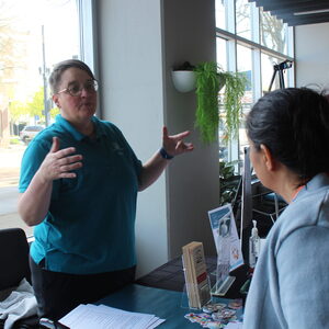 A group of people come around and listen to a speaker wearing a blue collared shirt, as she explains more about the work behind Upstream Access. 