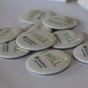 A pile of white circle badges, each with the words "I WILL" and the Providence Health logo printed 