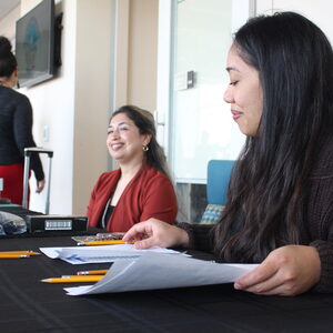 Two staff sit by a table with papers and pencils before them. 