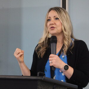 HHS Direct Mjere Simantel wears a black dress over a blue shirt, while speaking into a microphone. 