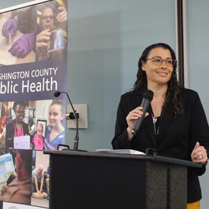 WCPH Division Manager Marie Boman-Davis wears a black dress while speaking into a microphone. 