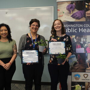 Three people stand ready for their picture, two of which hold plaque awards in their hands. 