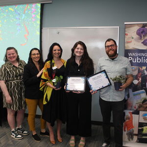Five people stand before the camera for their photo, two of which hold plaque awards in their hands. 