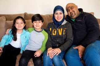Ahmed is sitting on a couch with his wife and two children.