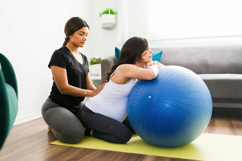 A 'douly' provider tends to a pregnant mom in an exercise with a fitness ball