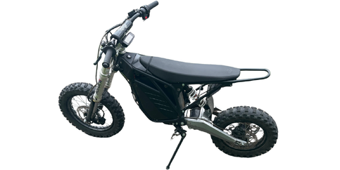 A black and silver electric dirt bike with knobby tires, a flat seat, and a kickstand, shown from the side