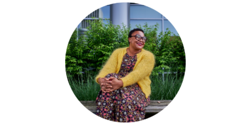 A female person wearing a yellow cardigan and multicolored dress sitting down.