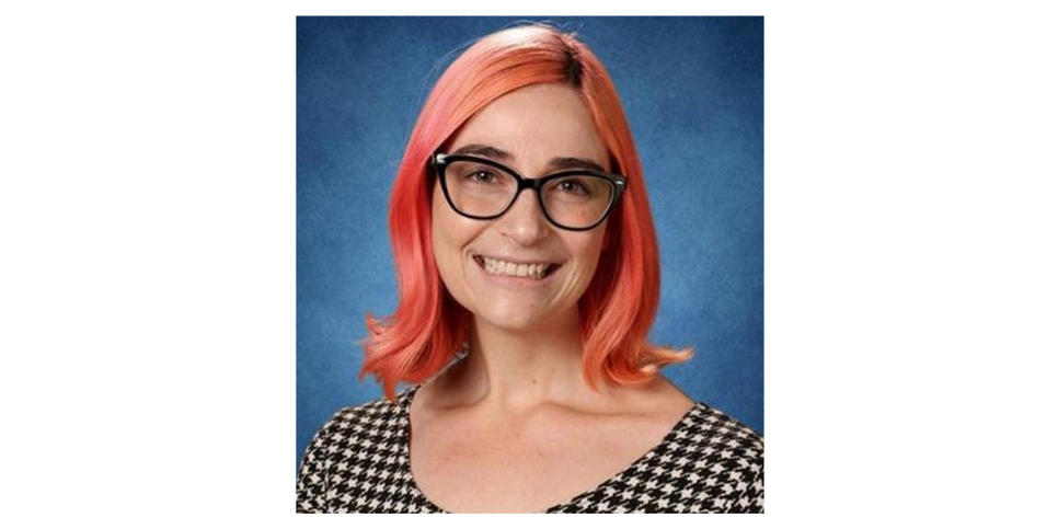 A woman with red hair wearing glasses and a black and white shirt. 