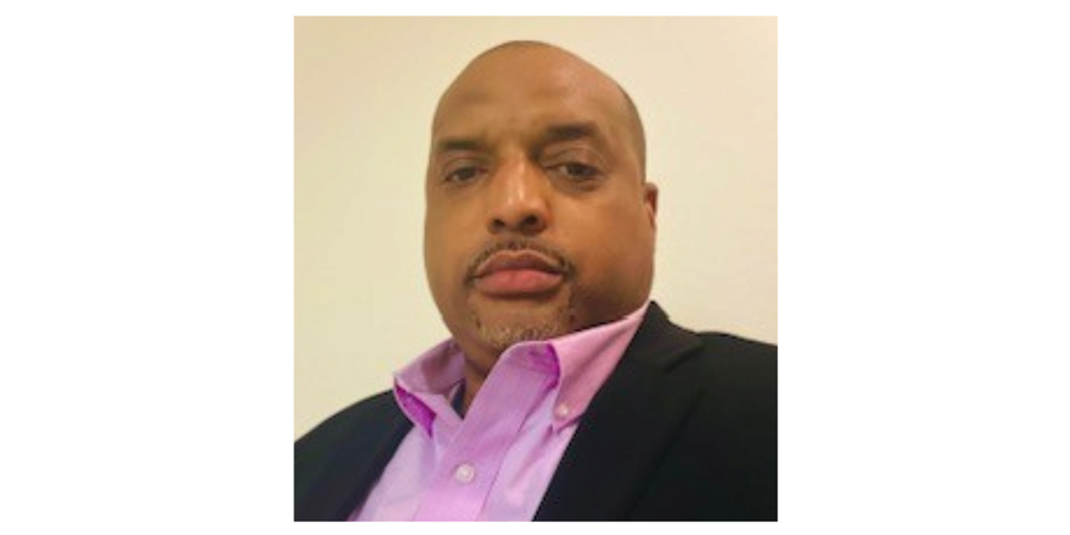 A man wearing a black blazer over a pink button up shirt. 