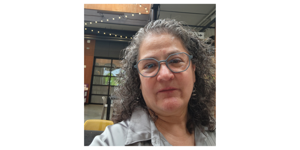A woman with gray hair wearing glasses and a gray shirt. 